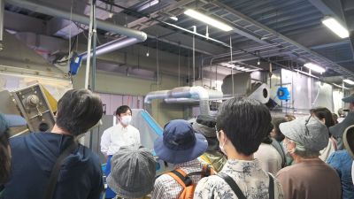 （写真）工場内で説明を聞く参加者たち