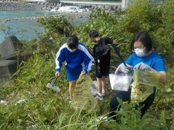 （写真）河原の草むらでペットボトルを拾う